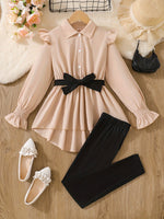 Elegant girl's outfit set with long sleeve peplum blouse and fitted pants on wood background.