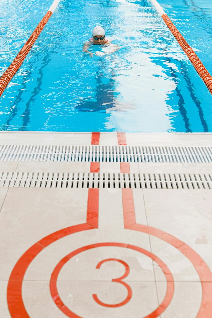 Un nageur s'entraînant dans une piscine intérieure avec la ligne 3 marquée, portant des lunettes et un bonnet de bain.