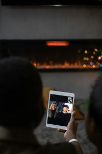 A couple enjoying a video call with friends on a tablet by a warm fireplace. Un couple profitant d'un appel vidéo avec des amis sur une tablette près d'une cheminée chaleureuse.