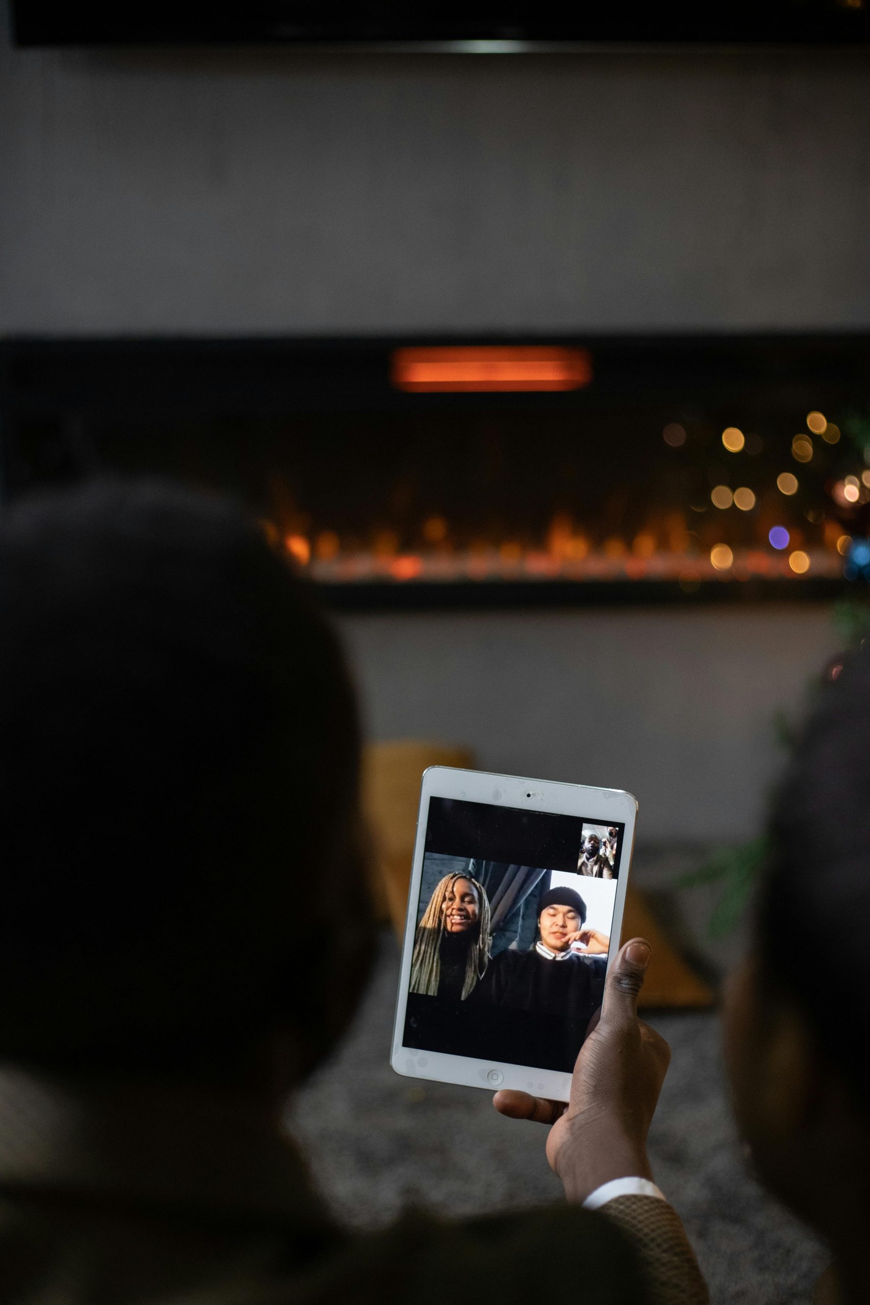 A couple enjoying a video call with friends on a tablet by a warm fireplace. Un couple profitant d'un appel vidéo avec des amis sur une tablette près d'une cheminée chaleureuse.