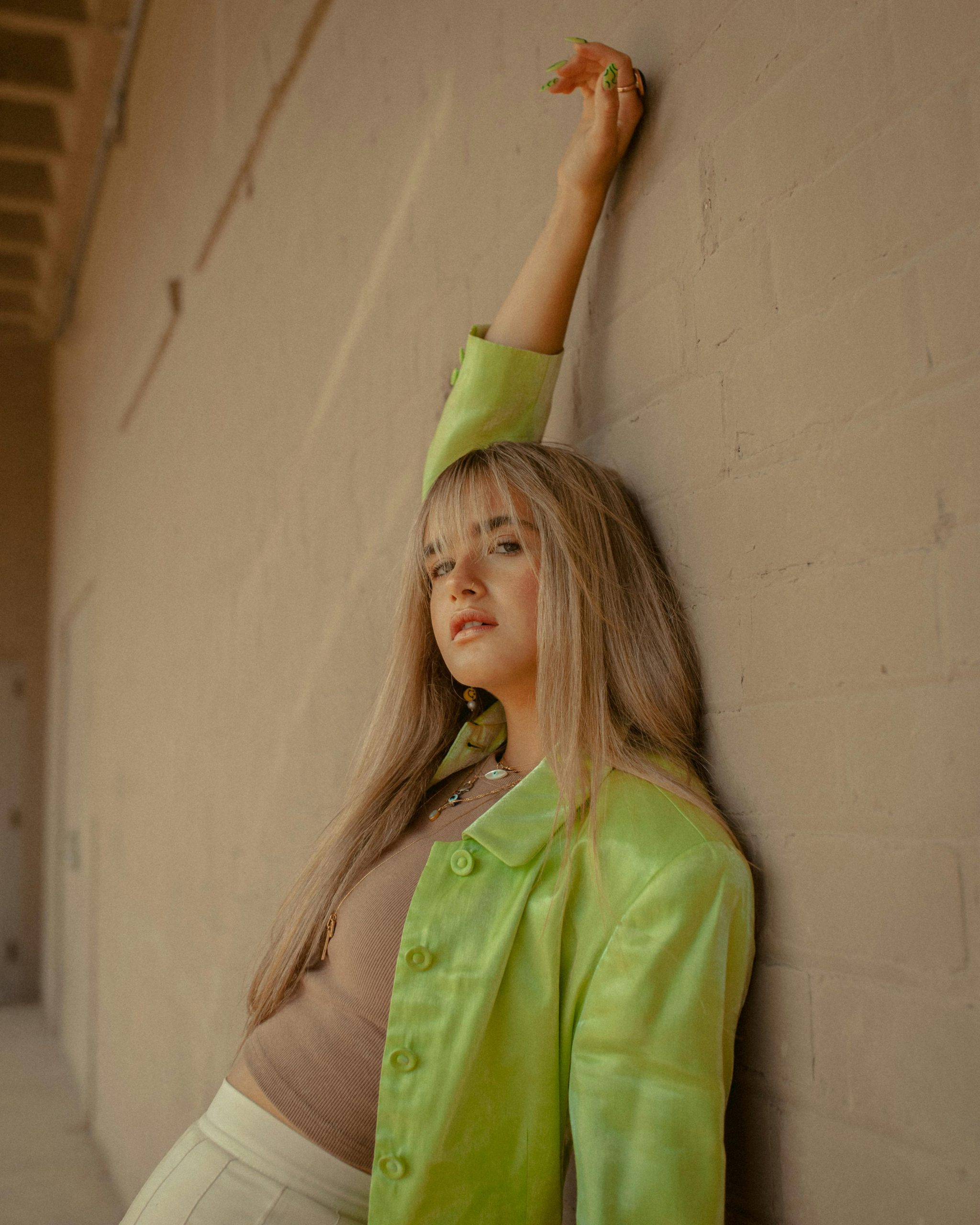 Femme adulte à la mode en blazer vert prenant la pose contre un mur, incarnant un style moderne