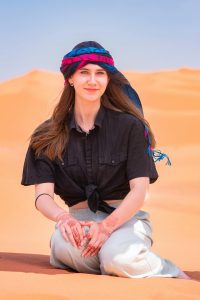 Une femme assise sur des dunes de sable à Merzouga, au Maroc, portant un foulard coloré et des tatouages au henné.