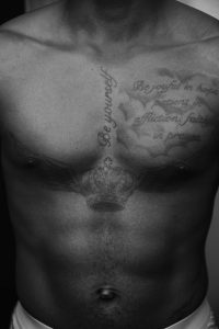 Gros plan d'un torse masculin avec des tatouages complexes sur la poitrine en noir et blanc.