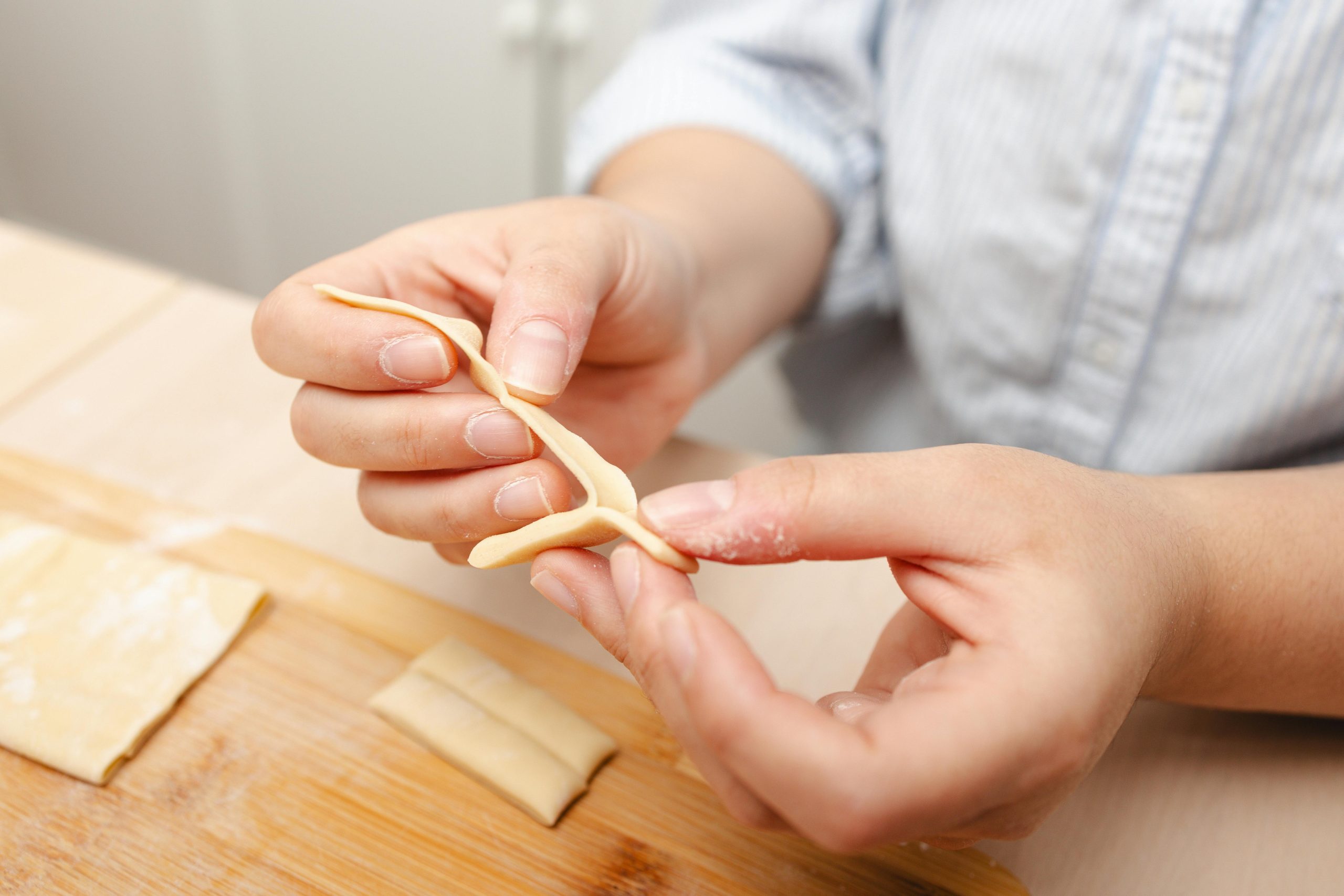 Hands skillfully shape fresh pasta dough on a wooden board in a cozy kitchen scene. Les mains façonnent avec habileté la pâte à pâtes fraîche sur une planche en bois dans une scène de cuisine douillette.