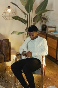 Casually dressed man sitting on a chair using a smartphone in a cozy room setting. Homme vêtu décontracté assis sur une chaise utilisant un smartphone dans un cadre de pièce douillet.