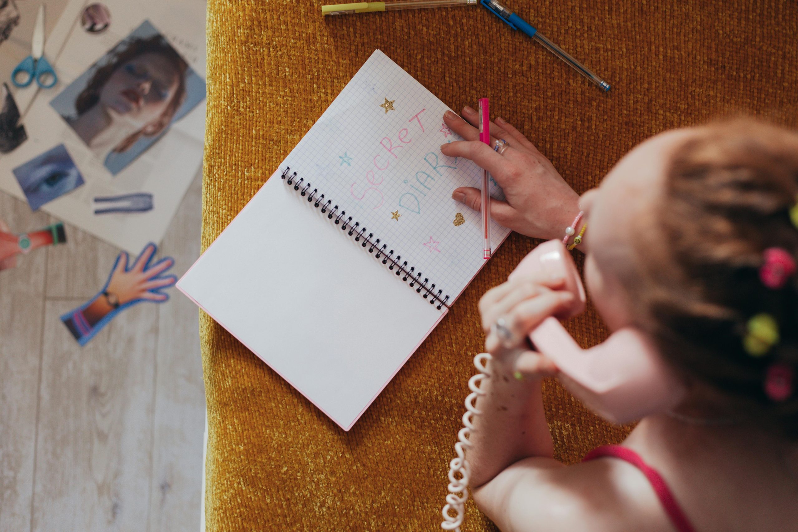 Woman writing in a diary while on a vintage pink phone, highlighting nostalgia and creativity. Une femme écrivant dans un journal intime tout en parlant sur un téléphone rose vintage, mettant en évidence la nostalgie et la créativité.
