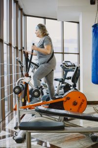 An adult woman using an elliptical trainer in a bright, modern gym. Une femme adulte utilisant un appareil elliptique dans une salle de sport moderne et lumineuse.