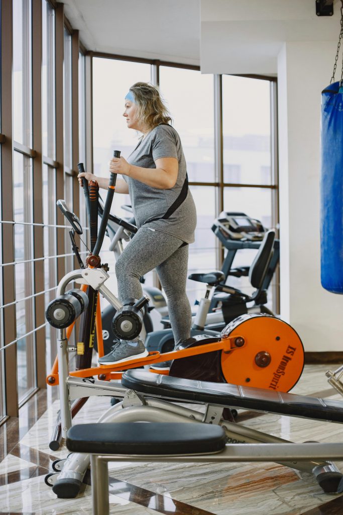 An adult woman using an elliptical trainer in a bright, modern gym. Une femme adulte utilisant un appareil elliptique dans une salle de sport moderne et lumineuse.