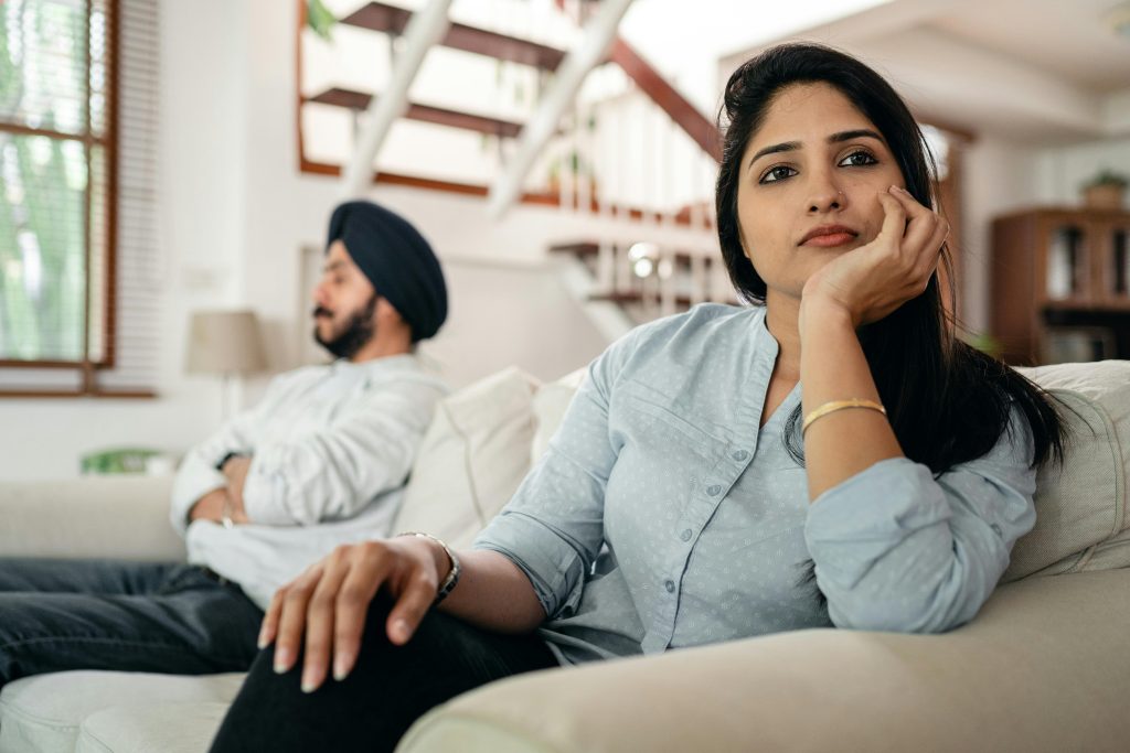 Young Indian couple sitting on different sides of couch and ignoring each other after arguing at home Un jeune couple indien assis de différents côtés du canapé s'ignorant mutuellement après une dispute à la maison