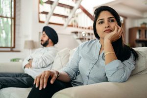 Young Indian couple sitting on different sides of couch and ignoring each other after arguing at home Un jeune couple indien assis de différents côtés du canapé s'ignorant mutuellement après une dispute à la maison