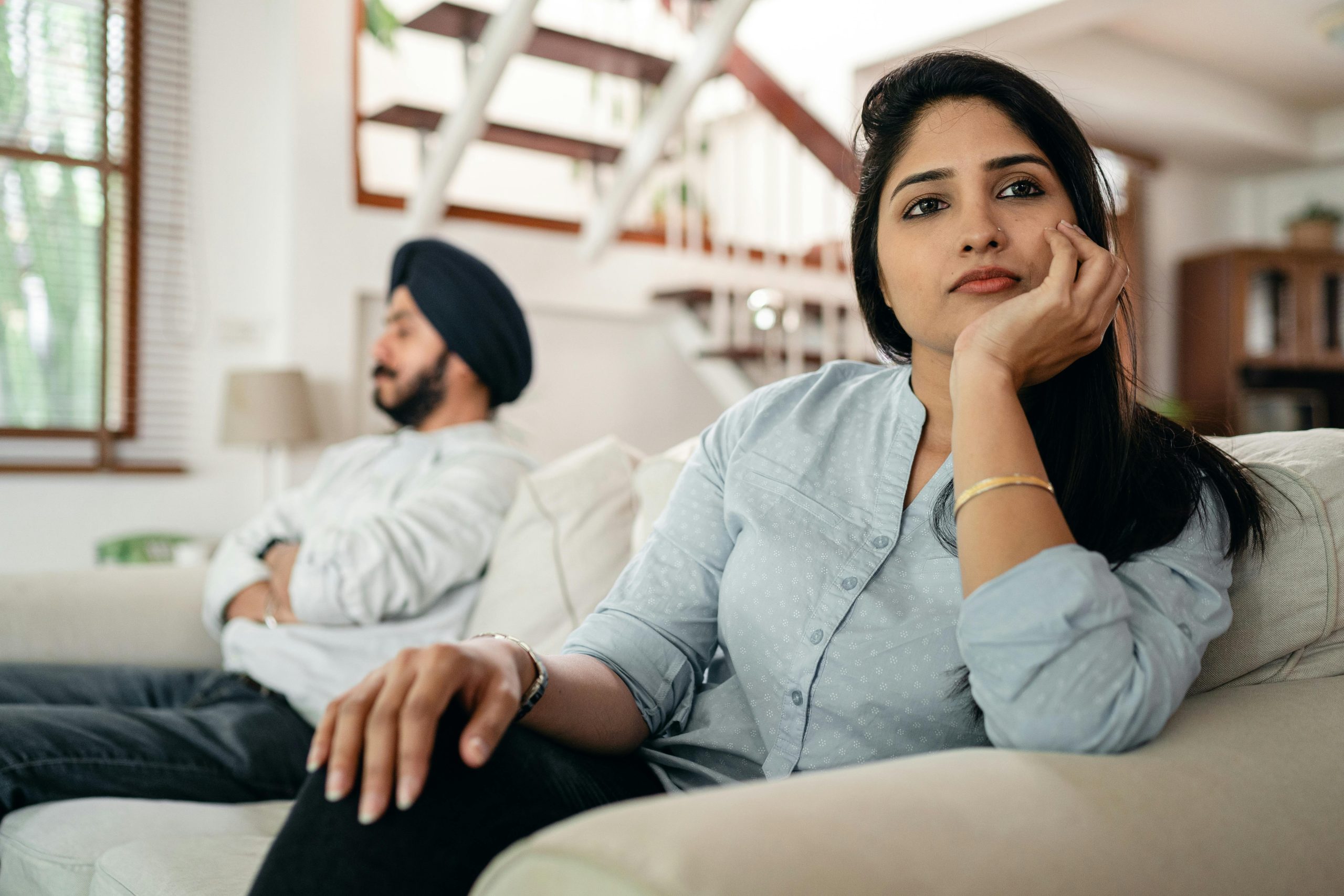 Young Indian couple sitting on different sides of couch and ignoring each other after arguing at home Un jeune couple indien assis de différents côtés du canapé s'ignorant mutuellement après une dispute à la maison