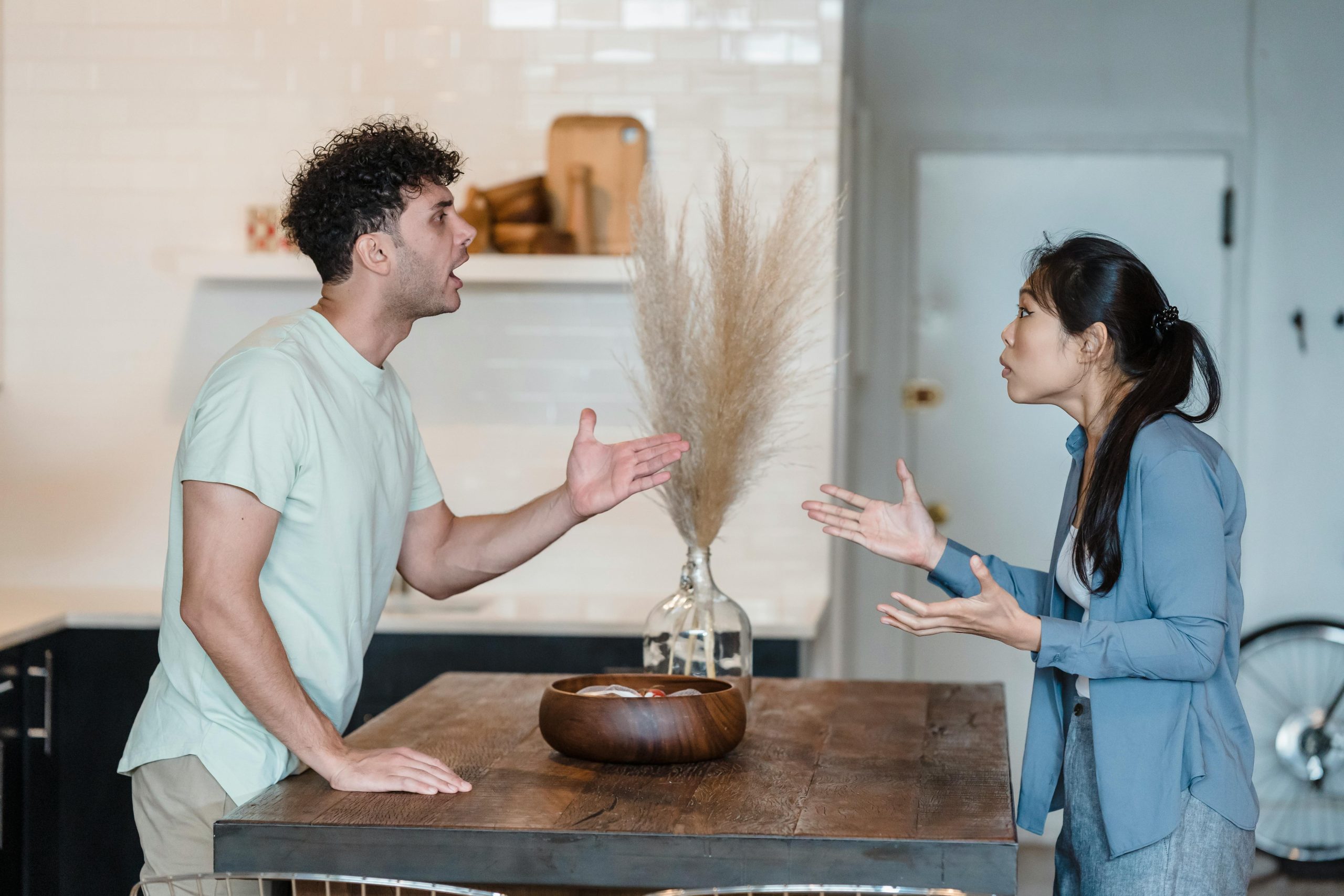 A couple engages in a heated argument at a wooden table in a modern indoor setting. Un couple engage une discussion animée à une table en bois dans un cadre intérieur moderne.
