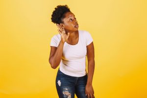 A confident African American woman poses with a listening gesture against a vibrant yellow background. Une femme afro-américaine confiante pose avec un geste d'écoute sur un fond jaune vibrant.