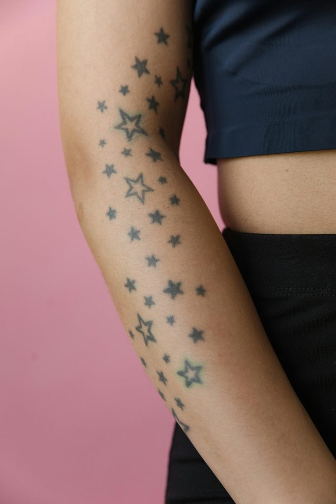 A close-up photo of an arm with star tattoos against a pink backdrop. Une photo en gros plan d'un bras avec des tatouages d'étoiles sur un fond rose.