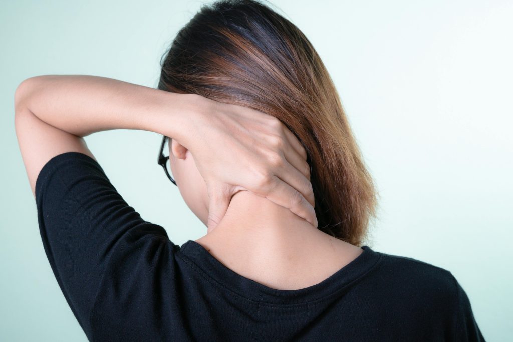 Rear view of a woman massaging her neck, depicting neck pain relief or self-care concepts. Vue arrière d'une femme se massant le cou, illustrant le soulagement de la douleur au cou ou les concepts d'auto-soins.