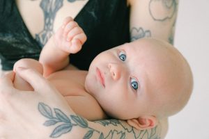 A beautiful baby with blue eyes held gently by tattooed arms, showcasing love and innocence. Un magnifique bébé aux yeux bleus tenu doucement par des bras tatoués, montrant l'amour et l'innocence.
