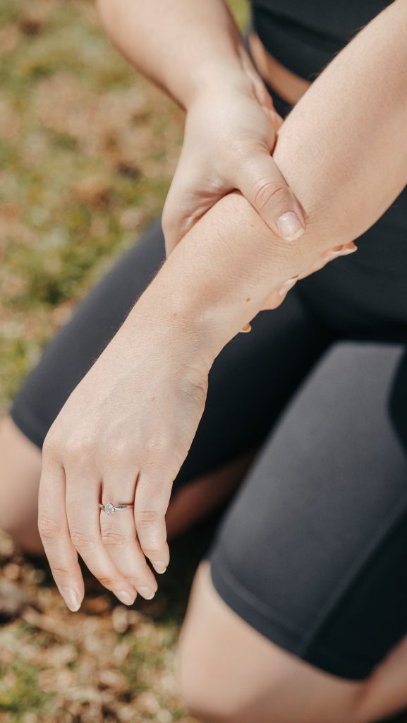 Close-up of a woman holding her wrist, indicating pain, while kneeling outdoors in athletic wear. Gros plan d'une femme se tenant le poignet, indiquant la douleur, tout en s'agenouillant à l'extérieur en tenue de sport.