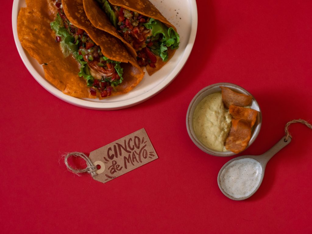 Delicious tacos and dips for a festive Cinco de Mayo celebration on vibrant red backdrop. Des tacos délicieux et des trempettes pour une célébration festive de la Cinco de Mayo sur un fond rouge vibrant.
